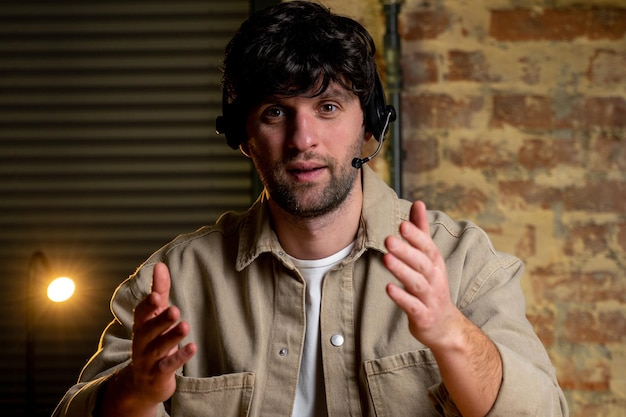 Businessman in wireless headphones makes a video call on a laptop looks at the camera Portrait of a young smiling employee support services in the headset looking at the camera