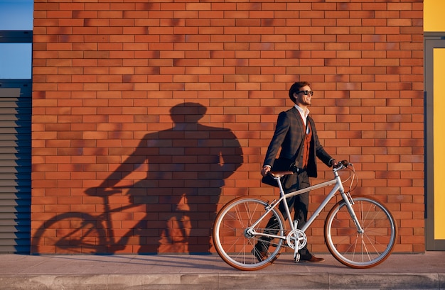 Businessman with bike walking near brick wall