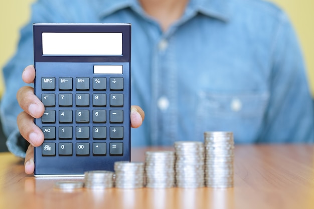 A businessman with a calculator and a stack of coins in foreground