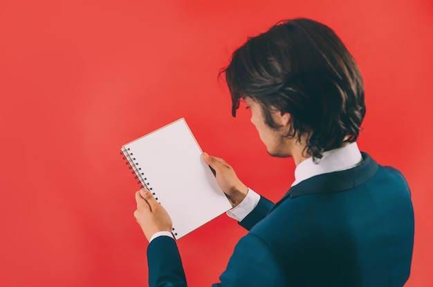 Businessman with a mock up notepad in his hands on a red space.