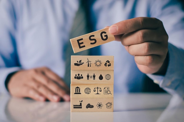 Businessman with wooden block on hand ESG icon concept for environmental social and governance in sustainable and ethical business on network connection on green background