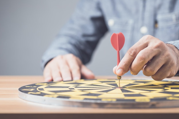 Businessman working in the office and throwing arrow darts in the center of yellow dartboard Goal and success for business concept