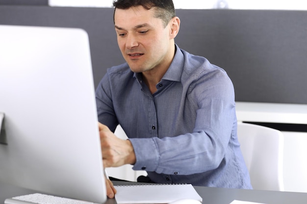 Businessman working with computer in modern office. Headshot of male entrepreneur or company director at workplace. Business concept.