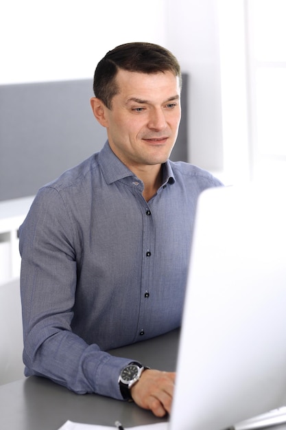 Businessman working with computer in modern office. Headshot of male entrepreneur or company director at workplace. Business concept.