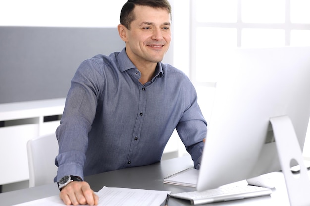 Businessman working with computer in modern office. Headshot of male entrepreneur or company director at workplace. Business concept.