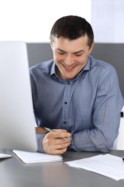 Businessman working with computer in modern office. Headshot of male entrepreneur or company director at workplace. Business concept.