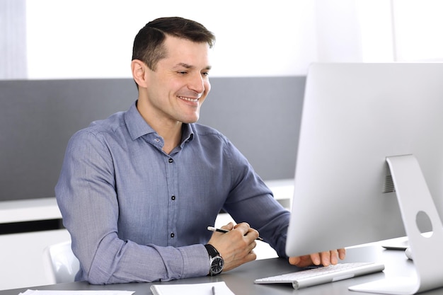 Businessman working with computer in modern office. Headshot of male entrepreneur or company director at workplace. Business concept.