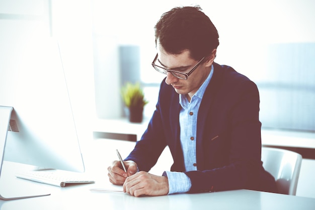 Businessman working with computer in modern office. Headshot of male entrepreneur or company manager at workplace. Business concept.