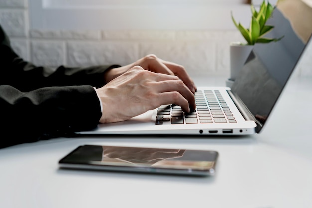 Businessman working with computer in office Man work on laptop at home with mobile phone on white desk Work from home business and technology concept Closeup copy space