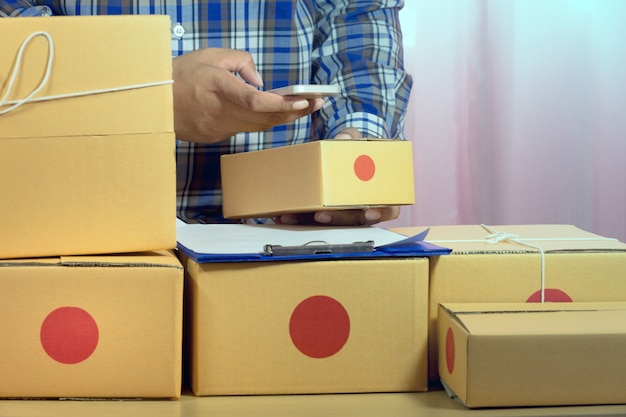 Businessman working with mobile phone and packing brown parcels box at home office