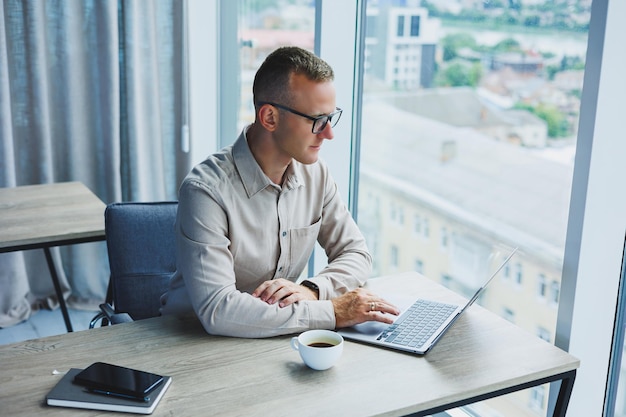 A businessman works on a laptop a manager sits at a table in the office works on a laptop Freelancer workplace employee at remote work Remote workplace in coworking cafe