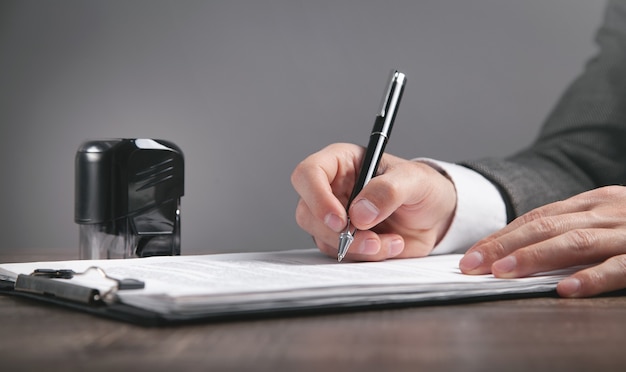 Businessman writing in document. Stamp on the desk