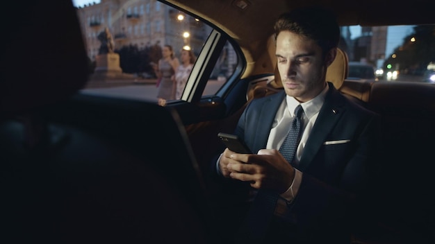 Businessman writing message on smartphone in car Man typing text on mobile