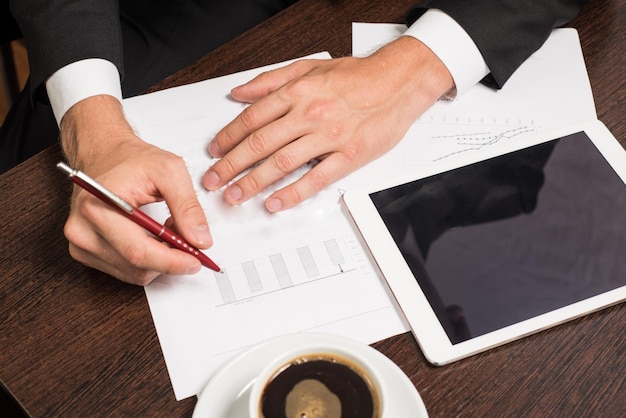 Businessman writing on the paper next to the tablet coffee cell phone