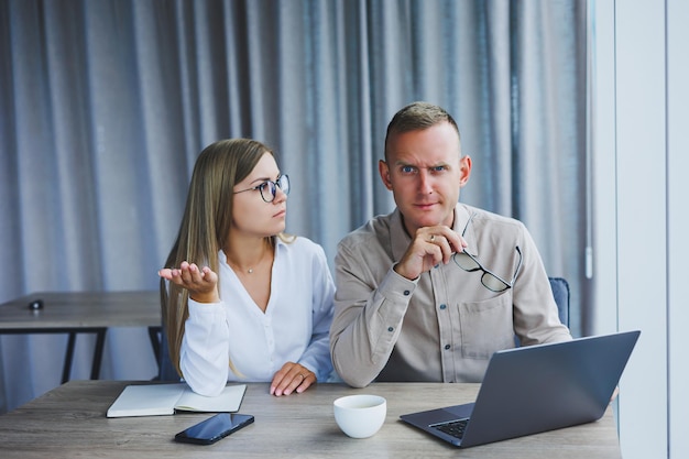 Businessmen are discussing while working with laptop in the office Focused business people cooperating in a modern workspace Two young businessmen are sitting together at a table