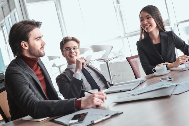 Businessmen and businesswoman at office working together sitting at table discussing project smiling joyful relaxed