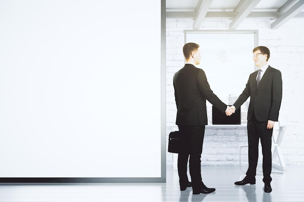 Businessmen shake hands in loft office with blank white wall mock up