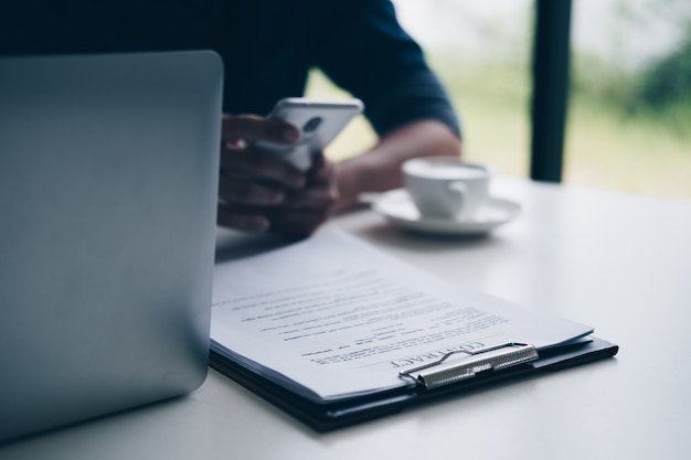 Businessmen using smartphone while sitting at desk with contract paper