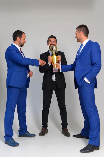 Businessmen with happy faces in formal suits hold golden prize