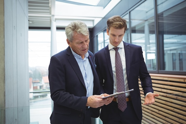 Businesspeople discussing over clipboard in the corridor