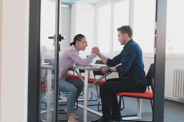 Businesspeople, rivalry and people concept - businesswoman and businessman arm wrestling during corporate meeting in modern bright open space coworking startup business office.