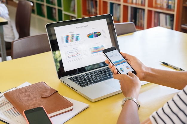 Businesswoman analyzing financial data on smartphone and computer screen.Close up