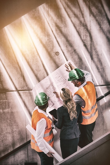 Businesswoman and architects standing on staircase discussing with blueprint