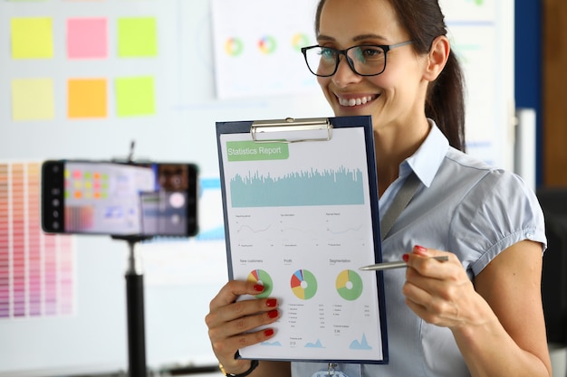 Businesswoman broadcasts videoconference to smartphone showing commercial performance.