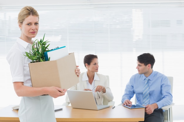 Businesswoman carrying her belongings with colleagues in background