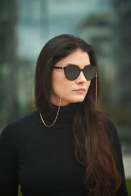 Businesswoman in the city A stylish and attractive caucasian lady wears fashionable dark sunglasses with chain accessories Outdoor portrait of a confident woman