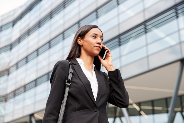 Businesswoman Commuting To Work Talking On Mobile Phone Outside Modern Office Building