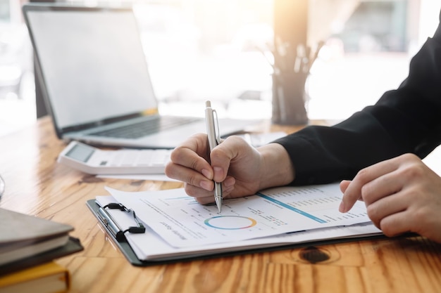 Businesswoman discussing analysis charts or graphs on desk table and using laptop computer. Close up female analysis and strategy concept.