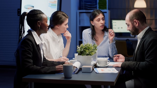 Businesswoman discussing management statistics working at corporate strategy in office meeting room. Diverse multi ethnic businesspeople coworkers brainstorming company ideas in evening