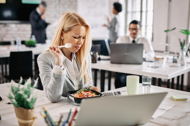 Businesswoman feeling disgusted by vegetable salad she is eating on lunch break in the office