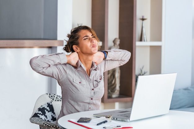 Businesswoman feeling pain in neck after sitting at the table with laptop.