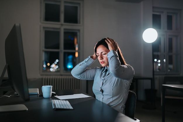 Businesswoman feeling unwell suffering from headache while working overtime.