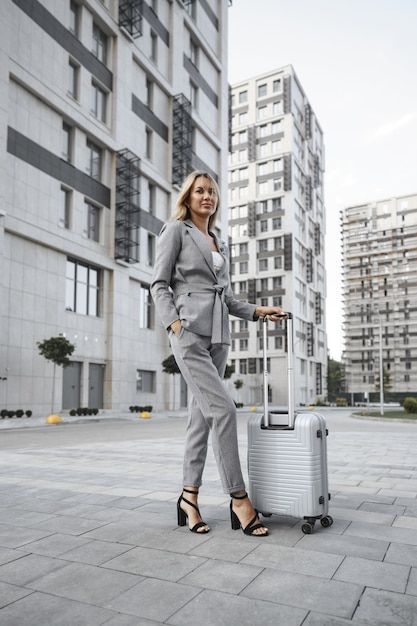 Businesswoman in gray suit on business trip walking with her luggage in the city