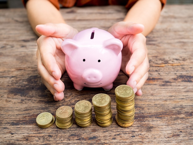 Businesswoman hand prevent  Pink piggy bank with gold coins pile Saving money for retirement fund