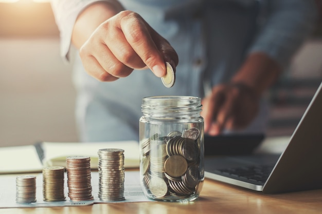 businesswoman hand puting coins in glass for saving money