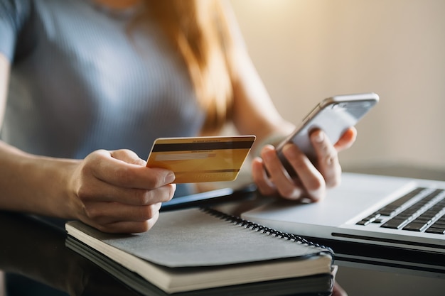 Businesswoman hand using smart phone, tablet payments and holding credit card online shopping, omni channel, digital tablet docking keyboard computer at office in sun light