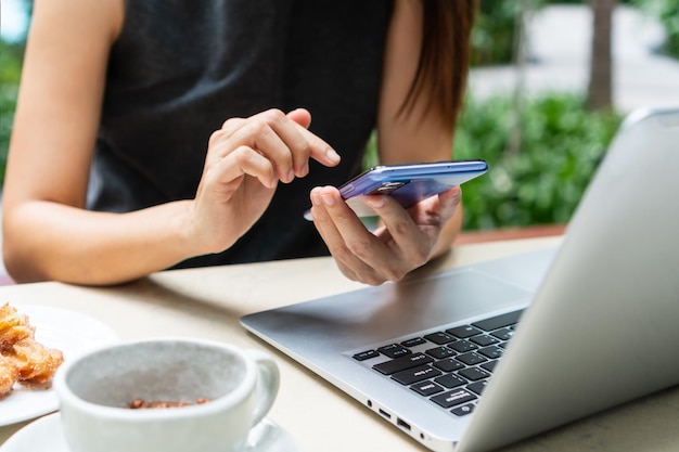 Businesswoman hands using mobile phone with laptop computer and snack on desk Work from home business and technology concept Closeup