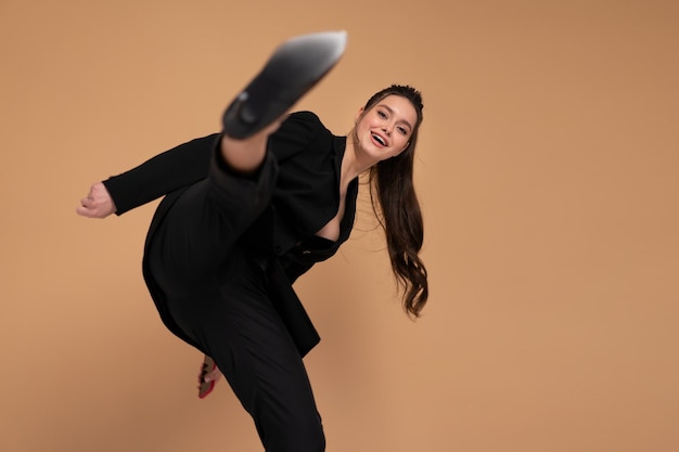 Businesswoman hitting with leg in camera dressed black office suit smile isolated on color background. Fight for business. Martial Art Karate pose in the studio on grey background. Kung fu style