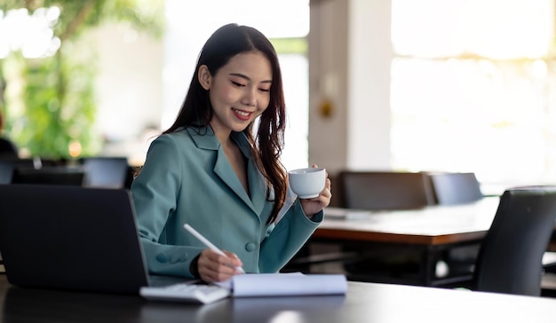 Businesswoman holding coffee cup and analyzing business online data in laptop computer.