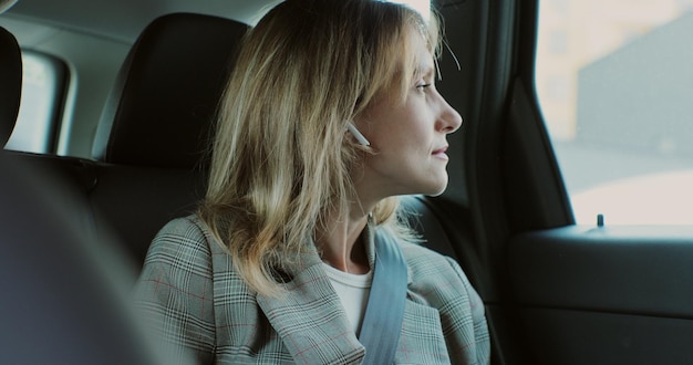 Businesswoman inserted wireless headphones into her ears in backseat car Young lady listening music in headphones