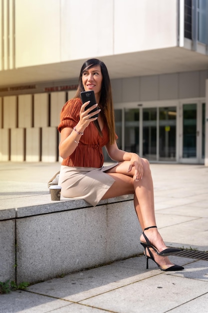 Businesswoman outside the office sending an email with the phone