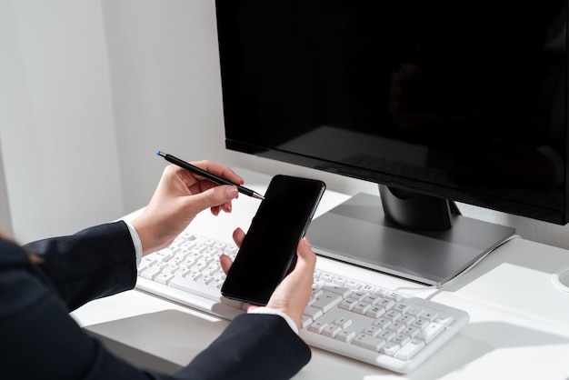 Businesswoman Pointing With Pen On Mobile Phone With Important Message Sitting On Desk With Computer Woman In Suit Having Cellphone With Crutial Informations