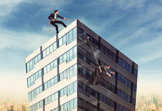 Businesswoman pulling businesswoman on the roof with a rope