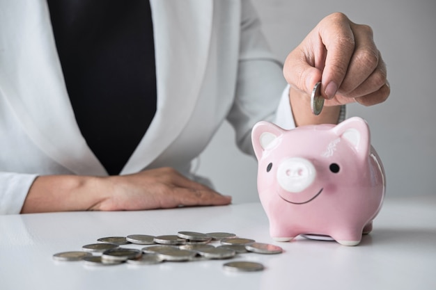 Businesswoman putting a coin into a piggy bank