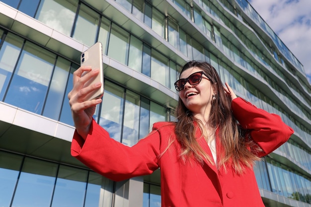 A businesswoman in a red stylish jacket during a video call with colleagues on the background of the office outside