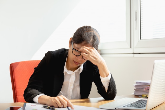 Businesswoman resting hands on head with eyes close at work desk in office.